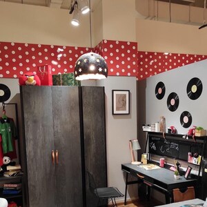 Może przedstawiać: Sypialnia z szarą i czarną szafą, czarnym biurkiem z blatem z tablicy kredowej, czarnym metalowym krzesłem i szarym łóżkiem z czarno-białą poduszką w kształcie galaktyki. Ściany są ozdobione czerwonymi i białymi kropkami oraz czarnymi płytami winylowymi.