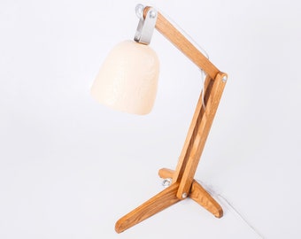 May include: A wooden desk lamp with a white shade and a white cord. The lamp has a flexible arm and a tripod base.