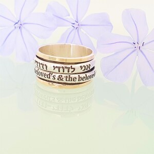 May include: A silver and gold spinning ring with the Hebrew words "Ani L'dodi" and "Ve'dodi Li" engraved on it, which translate to "I am my beloved's & the beloved is mine".