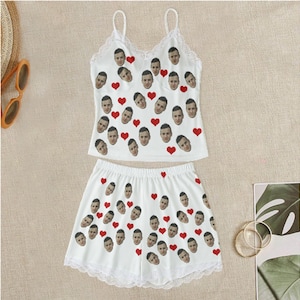 Könnte beinhalten: Weißer Schlafanzug mit rotem Herz- und Gesichtsdruck. Das Oberteil hat Spaghettiträger und einen Spitzenbesatz. Die Shorts haben einen Spitzenbesatz und einen elastischen Bund.