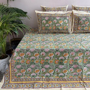 Puede incluir: Una sábana de cama verde con un patrón floral en tonos de rosa, amarillo y marrón. La sábana tiene un borde amarillo y marrón.