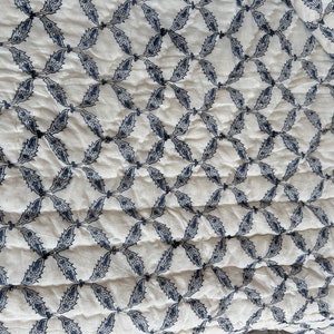 K&ouml;nnte beinhalten: Wei&szlig;er Stoff mit einem sich wiederholenden Muster aus blauen, stilisierten Bl&auml;ttern in einer Diamantform.