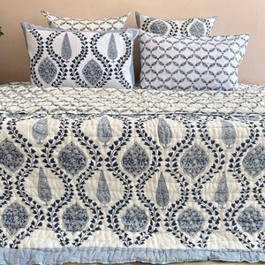 K&ouml;nnte beinhalten: Eine wei&szlig;e und blaue gemusterte Bettdecke mit einem blauen und wei&szlig;en gemusterten Kissen darauf. Die Bettdecke hat ein florales Design mit einem Paisley-Muster.