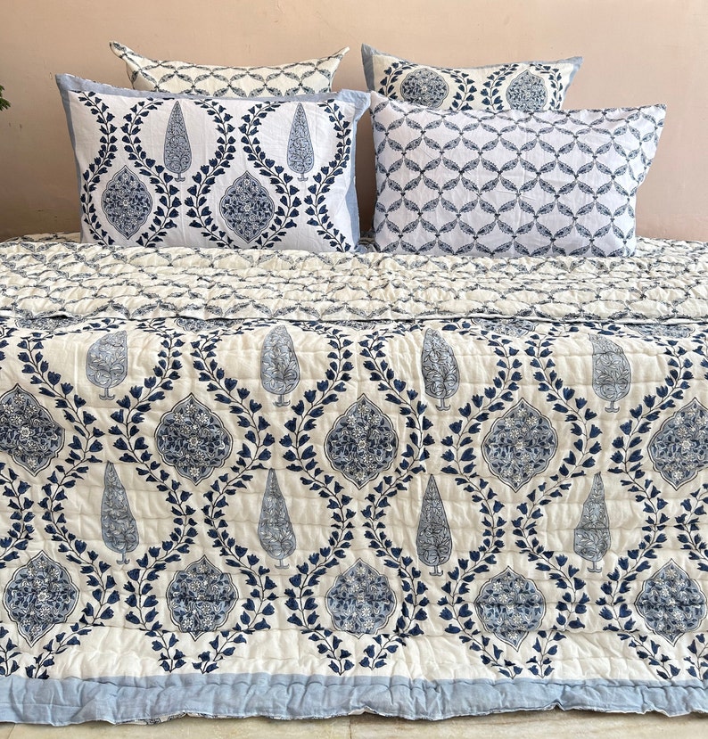 K&ouml;nnte beinhalten: Eine wei&szlig;e und blaue gemusterte Bettdecke mit einem blauen und wei&szlig;en gemusterten Kissen darauf. Die Bettdecke hat ein florales Design mit einem Paisley-Muster.