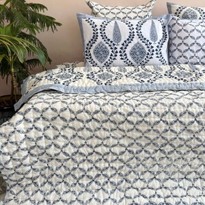 K&ouml;nnte beinhalten: Eine wei&szlig;e und blaue Steppdecke mit geometrischem Muster. Die Steppdecke ist aus Baumwolle und perfekt, um jedem Schlafzimmer einen Hauch von Stil zu verleihen.