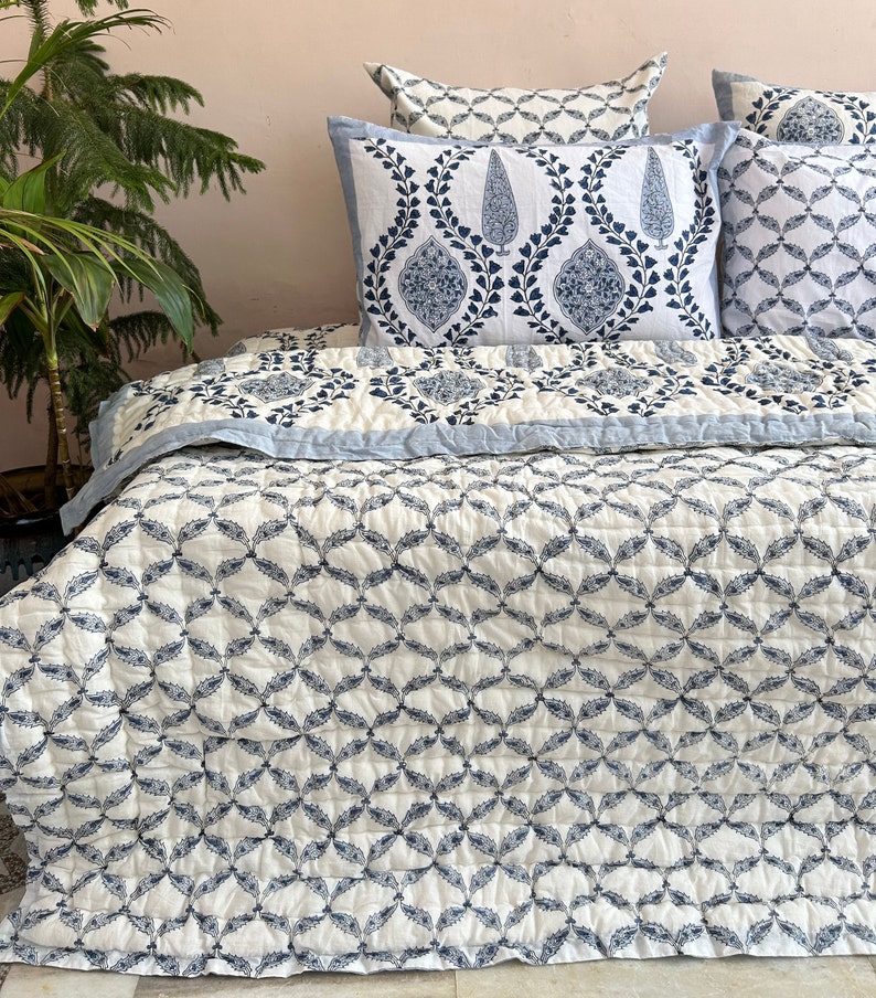 K&ouml;nnte beinhalten: Eine wei&szlig;e und blaue Steppdecke mit geometrischem Muster. Die Steppdecke ist aus Baumwolle und perfekt, um jedem Schlafzimmer einen Hauch von Stil zu verleihen.
