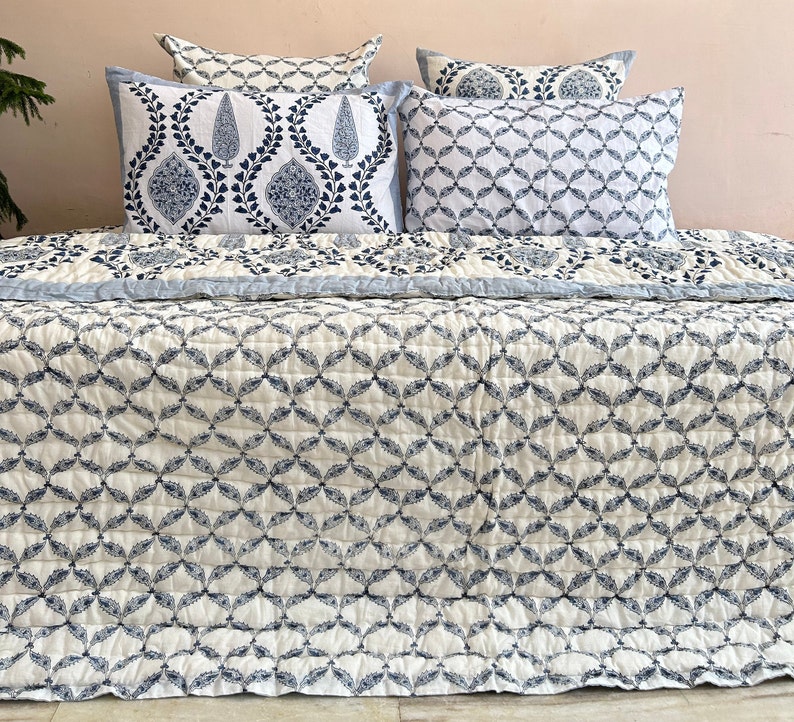 K&ouml;nnte beinhalten: Eine wei&szlig;e und blaue Steppdecke mit geometrischem Muster. Die Steppdecke ist aus Baumwolle und f&uuml;hlt sich weich und bequem an. Die Steppdecke ist perfekt, um jedem Schlafzimmer einen Hauch von Stil zu verleihen.