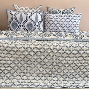 K&ouml;nnte beinhalten: Eine wei&szlig;e und blaue Steppdecke mit geometrischem Muster. Die Steppdecke liegt auf einem Bett mit passenden Kissenbez&uuml;gen und Kissen.