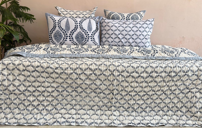 K&ouml;nnte beinhalten: Eine wei&szlig;e und blaue Steppdecke mit geometrischem Muster. Die Steppdecke liegt auf einem Bett mit passenden Kissenbez&uuml;gen und Kissen.