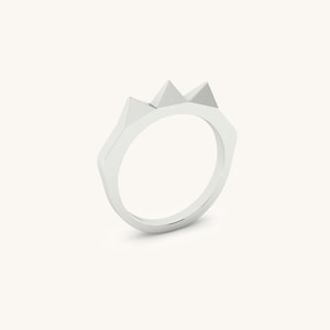 May include: A silver ring with three triangular points on the top. The ring is made of a smooth, polished metal.