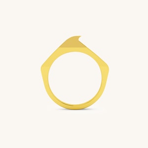 May include: A gold ring with a unique, angular design. The ring is made of a smooth, polished metal and has a sharp, pointed edge.