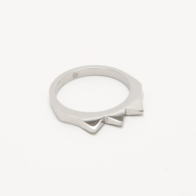K&ouml;nnte beinhalten: Ein silberner Ring mit einem spitzen, gezackten Randdesign.