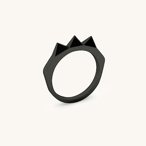K&ouml;nnte beinhalten: Ein schwarzer Ring mit einem dreieckigen Design auf der Oberseite. Der Ring ist aus Metall und hat eine glatte Oberfl&auml;che.