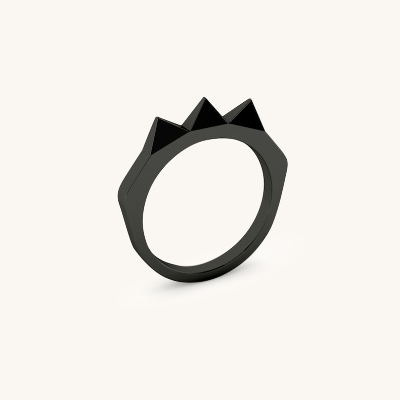 K&ouml;nnte beinhalten: Ein schwarzer Ring mit einem dreieckigen Design auf der Oberseite. Der Ring ist aus Metall und hat eine glatte Oberfl&auml;che.
