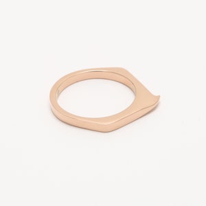 May include: A rose gold ring with a unique, angular design. The ring is made of a smooth, polished metal and has a slightly pointed edge.