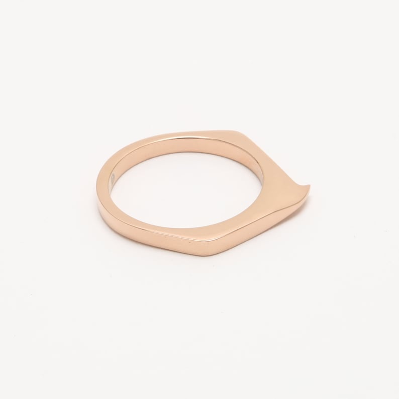 May include: A rose gold ring with a unique, angular design. The ring is made of a smooth, polished metal and has a slightly pointed edge.