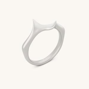 May include: A minimalist silver ring with a unique, flowing design. The ring features a smooth, curved band that rises to form a stylized, pointed shape. The ring is shown on a white background.