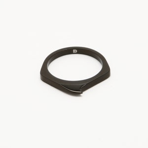 May include: A black ring with a pointed edge and a small "D" engraved on the inside.