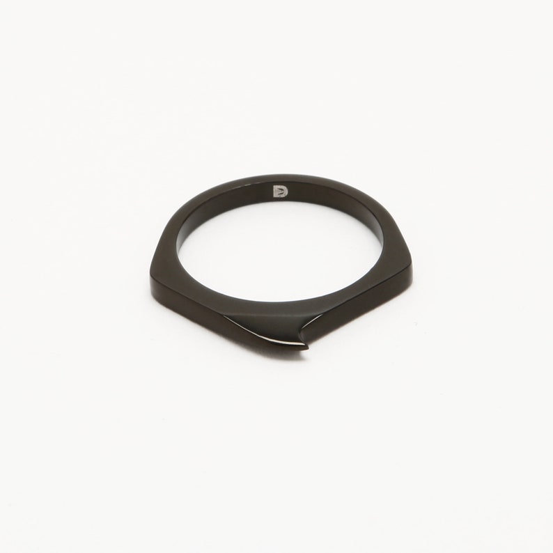 May include: A black ring with a pointed edge and a small "D" engraved on the inside.