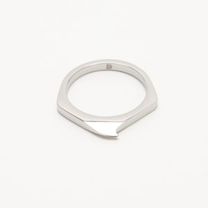 May include: A silver ring with a sharp, pointed edge. The ring is made of metal and has a simple, modern design.