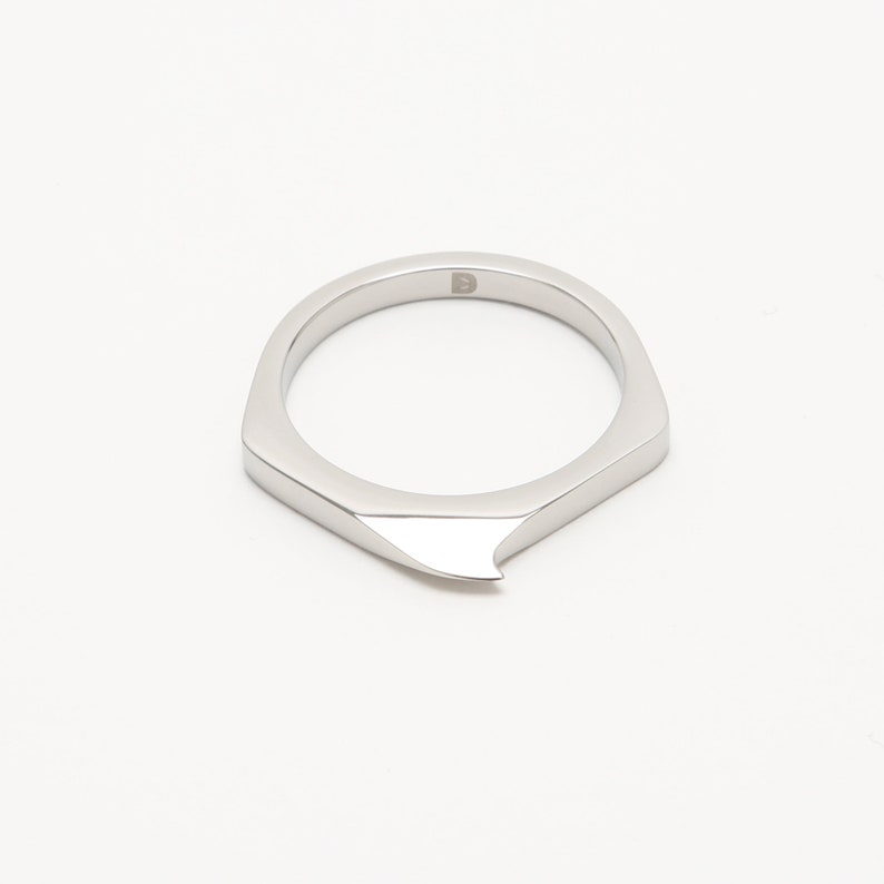May include: A silver ring with a sharp, pointed edge. The ring is made of metal and has a simple, modern design.