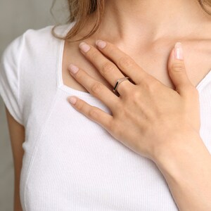 May include: A silver ring with a geometric design. The ring is on a person's finger.