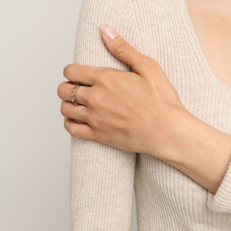 K&ouml;nnte beinhalten: Ein silberner Ring mit einem spitzen, geometrischen Design. Der Ring wird am Zeigefinger einer Hand getragen.