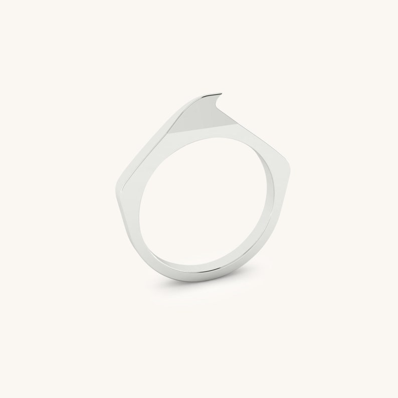 May include: A silver ring with a unique, angular design. The ring is made of a smooth, polished metal and has a sharp, pointed edge.