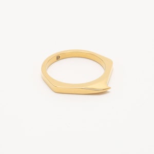 May include: A gold-colored ring with a pointed, angular design. The ring is made of metal and has a simple, modern style.