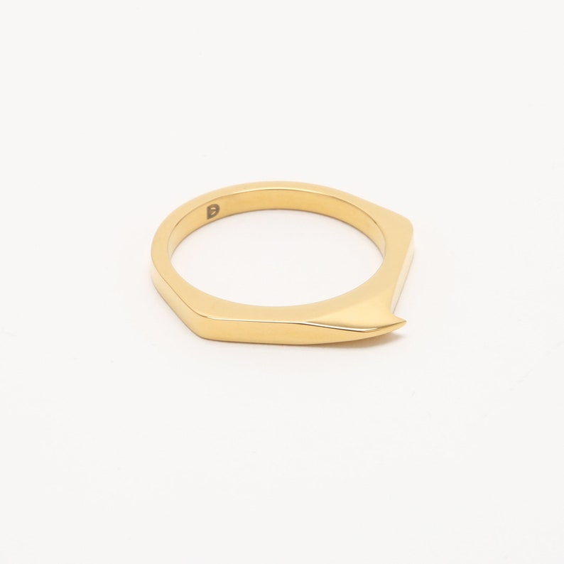 May include: A gold-colored ring with a pointed, angular design. The ring is made of metal and has a simple, modern style.