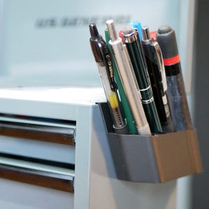 Peut inclure: Une boîte à outils US GENERAL bleu clair avec plusieurs tiroirs, contenant divers stylos et marqueurs dans un porte-stylo gris. La boîte à outils porte l'inscription "US GENERAL" sur le devant.