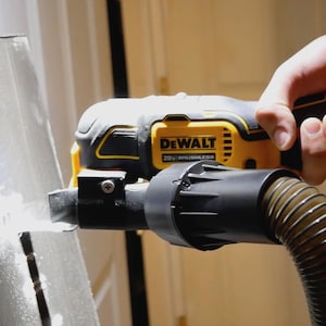 Puede incluir: Una multiherramienta oscilante DEWALT 20V BRUSHLESS amarilla y negra se utiliza para cortar una lámina de metal. La herramienta tiene una manguera negra. La herramienta es sostenida por una persona.