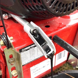 May include: Close-up of a red Troy-Bilt engine with black oil draining from a spout. The oil is dark and viscous, flowing into a black container. The engine has a black top and a silver dipstick. A parts list is visible.