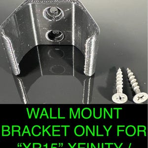 Könnte beinhalten: Eine schwarze Wandhalterung für eine "XR15" Xfinity / Cox Fernbedienung, mit zwei silbernen Schrauben. Die Halterung hat ein gebogenes Design mit zwei Löchern, und das Xfinity-Logo ist oben rechts sichtbar. Der Text unten lautet "WALL MOUNT BRACKET ONLY FOR "XR15" XFINITY / COX REMOTE".