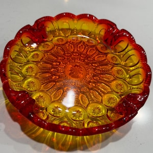 May include: A red and yellow glass ashtray with a scalloped edge and a textured, patterned design.