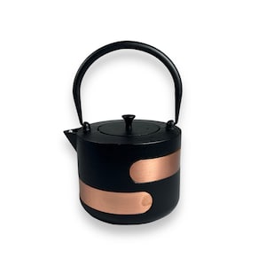 Könnte beinhalten: Schwarze Gusseisen-Teekanne mit einem Kupferband um die Mitte. Die Teekanne hat einen schwarzen Griff und einen schwarzen Deckel mit einem kleinen Knopf.