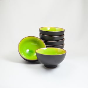 May include: A stack of six small, black bowls with a green interior. The bowls are stacked in a pyramid shape, with the top bowl being the largest and the bottom bowl being the smallest.