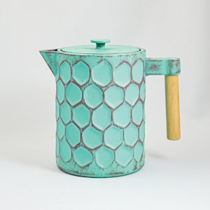 May include: A teal blue ceramic teapot with a honeycomb pattern and a wooden handle.