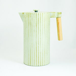 Könnte beinhalten: Eine hellgrüne Keramik-French-Press-Kaffeemaschine mit einem Holzgriff. Die Kaffeemaschine hat ein geripptes Design.