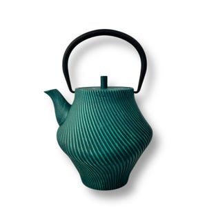 Könnte beinhalten: Eine türkisfarbene Teekanne mit schwarzem Griff und Deckel. Die Teekanne hat ein strukturiertes, geripptes Design. Der Griff ist gebogen und der Ausguss ist gebogen. Die Teekanne ist zum Aufbrühen von Tee bestimmt.