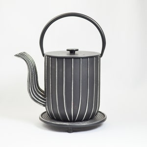 May include: Black cast iron teapot with a white striped design and a black handle. The teapot sits on a black metal stand with three legs.