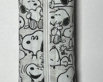 May include: A white zippered pouch with a black and white print of Snoopy characters. The pouch is made of fabric and has a zipper closure.