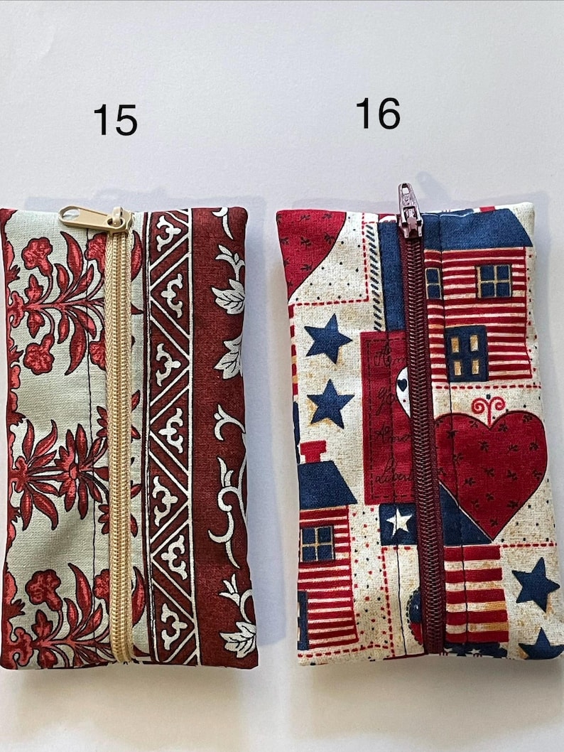 May include: Two rectangular fabric pouches with zips. Pouch 15 features a light green and dark red floral pattern with a gold zip. Pouch 16 displays a red, white, and blue patriotic print with houses, hearts, and stars, featuring a dark red zip.