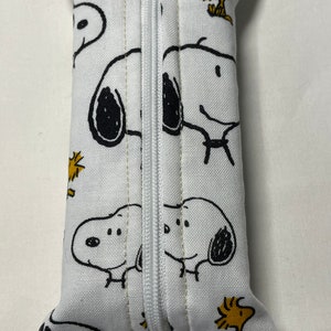 Pu&ograve; includere: Borsa bianca con cerniera a tema Peanuts. La borsa &egrave; rivestita in tessuto bianco con immagini di cartoni animati neri e gialli di Snoopy e Woodstock.