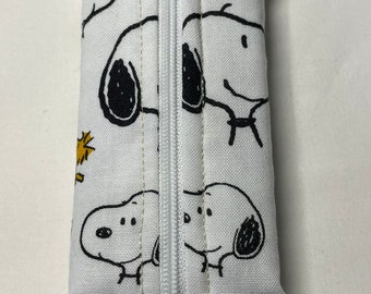 Op de afbeelding: Witte ritszak met een Peanuts-thema. De zak is bedekt met een witte stof met zwarte en gele cartoonafbeeldingen van Snoopy en Woodstock.