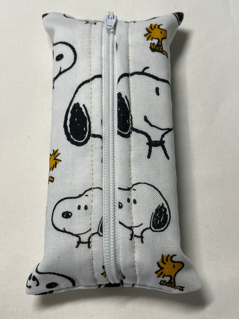 Pu&ograve; includere: Borsa bianca con cerniera a tema Peanuts. La borsa &egrave; rivestita in tessuto bianco con immagini di cartoni animati neri e gialli di Snoopy e Woodstock.
