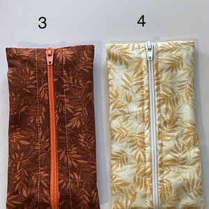 May include: Two rectangular fabric pouches labelled 3 and 4. Pouch 3 is dark brown with a leaf pattern and an orange centre zip. Pouch 4 is cream with a yellow leaf pattern and a white centre zip. Both pouches feature a vertical zip closure.