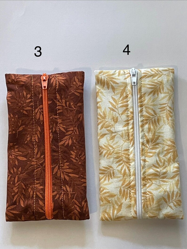 May include: Two rectangular fabric pouches labelled 3 and 4. Pouch 3 is dark brown with a leaf pattern and an orange centre zip. Pouch 4 is cream with a yellow leaf pattern and a white centre zip. Both pouches feature a vertical zip closure.