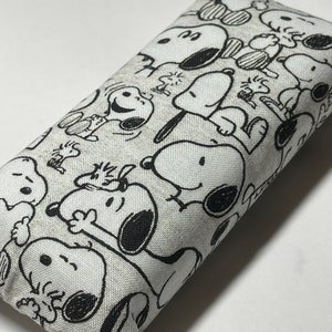 Op de afbeelding: Een wit stoffen etui met een zwart-witte print van Snoopy-figuren. Het etui is rechthoekig en heeft een ritssluiting.