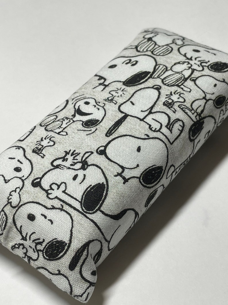 Op de afbeelding: Een wit stoffen etui met een zwart-witte print van Snoopy-figuren. Het etui is rechthoekig en heeft een ritssluiting.